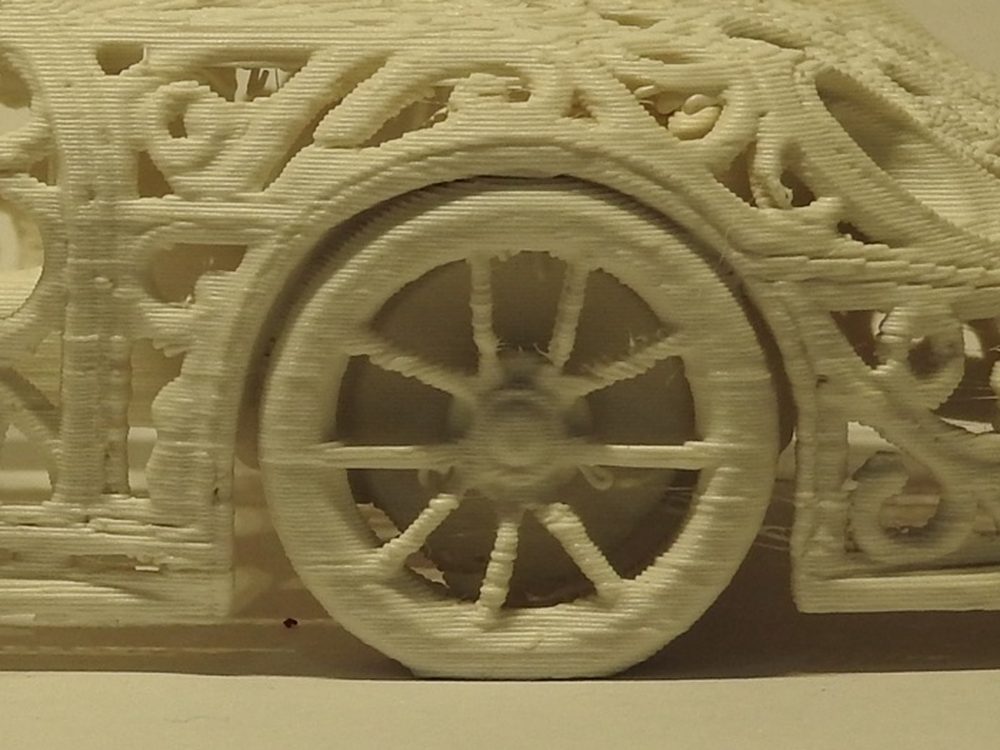 Close up of a printed ten spoke racing wheel under a lattice wheel arch, with the horizontal layer lines of the print clearly visible