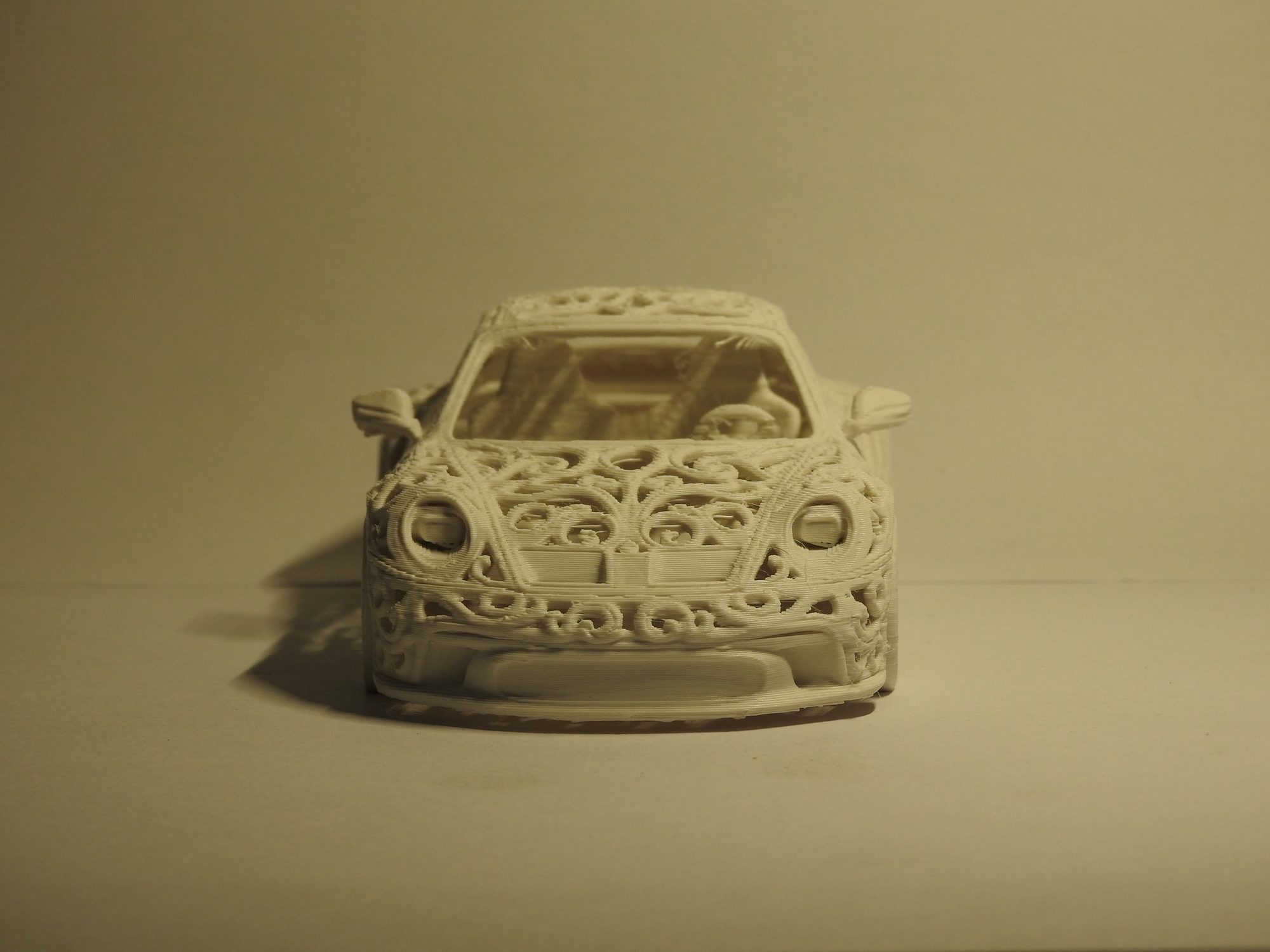 Ivory 3D printed Porsche 992 GT3 seen head on, with round headlights set into a symmetrical lattice across the hood and front bumper