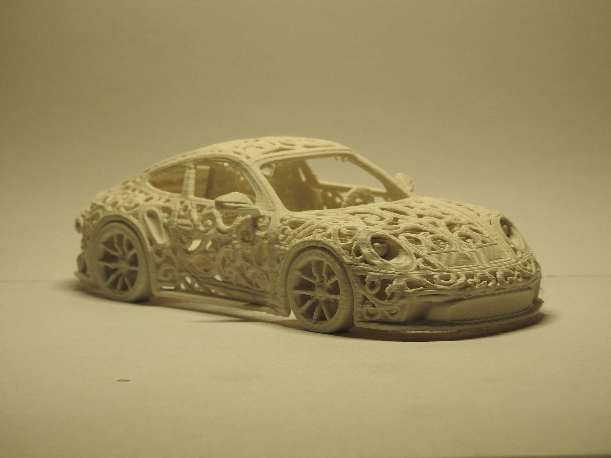 Ivory 3D printed Porsche 992 GT3 seen low from the front left, with the lattice wrapping the hood, door and wheel arches