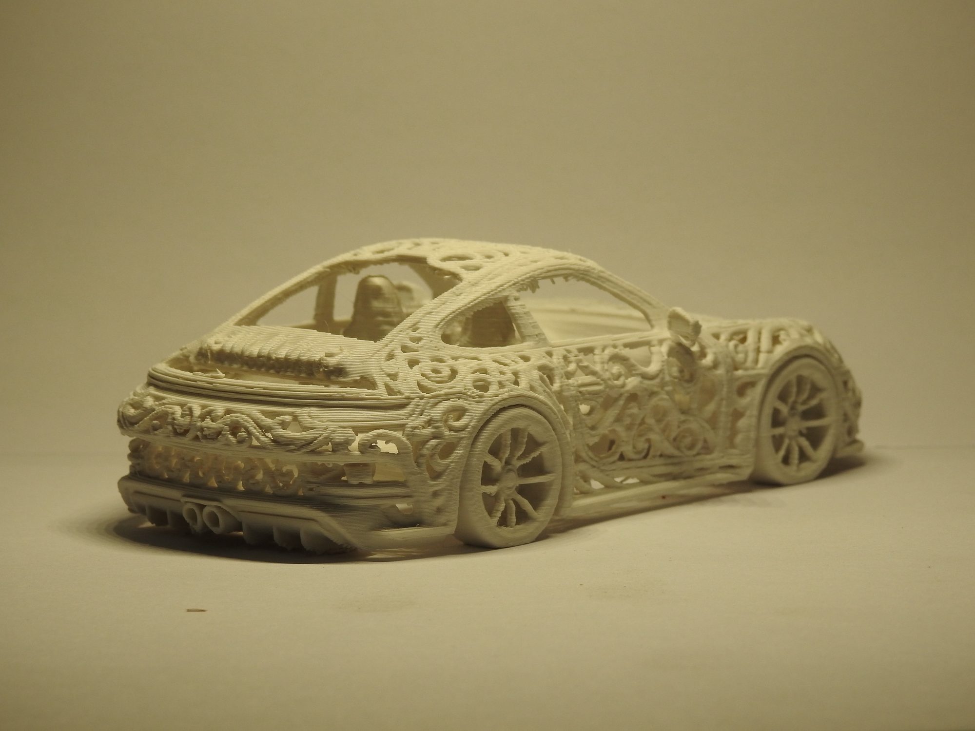 Ivory 3D printed Porsche 992 GT3 seen low from the rear left, showing the twin exhaust tips, lattice rear end and the seats through the rear window