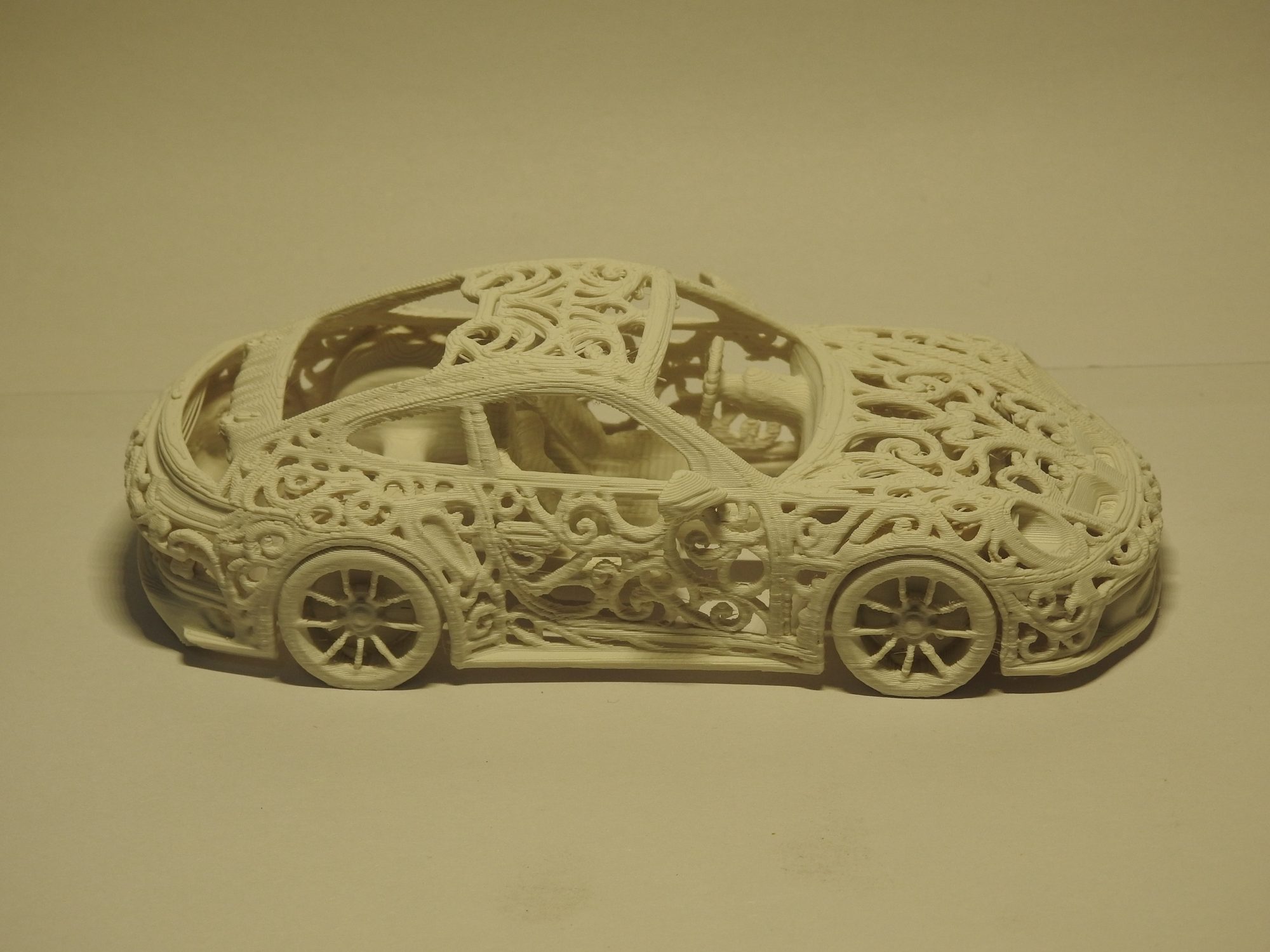 Ivory 3D printed Porsche 992 GT3 in left side profile, shot slightly from above, showing the open lattice roof and the interior through the windows