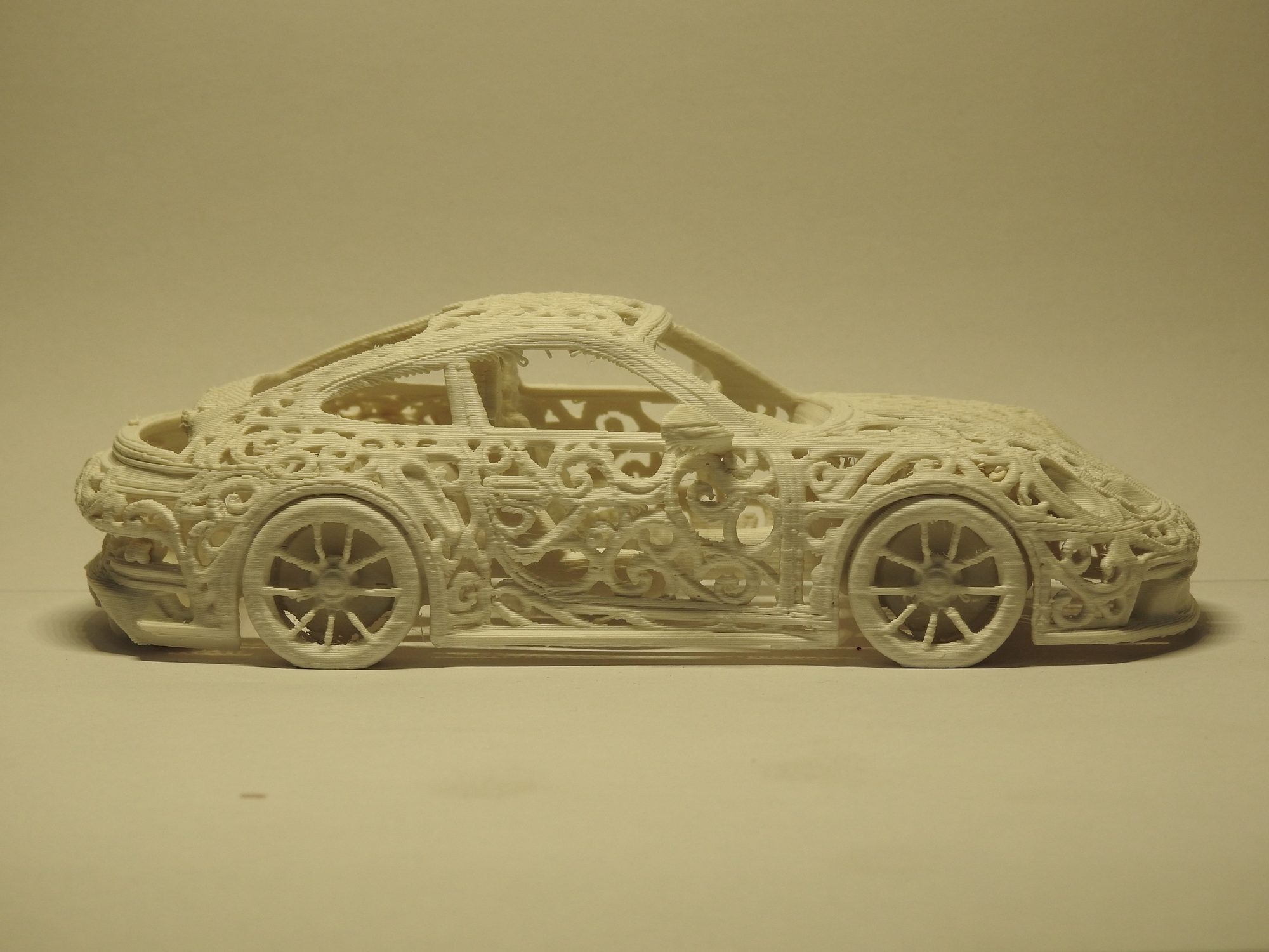 Ivory 3D printed Porsche 992 GT3 in left side profile at eye level, with racing wheels, wide arches and curling openwork along the doors